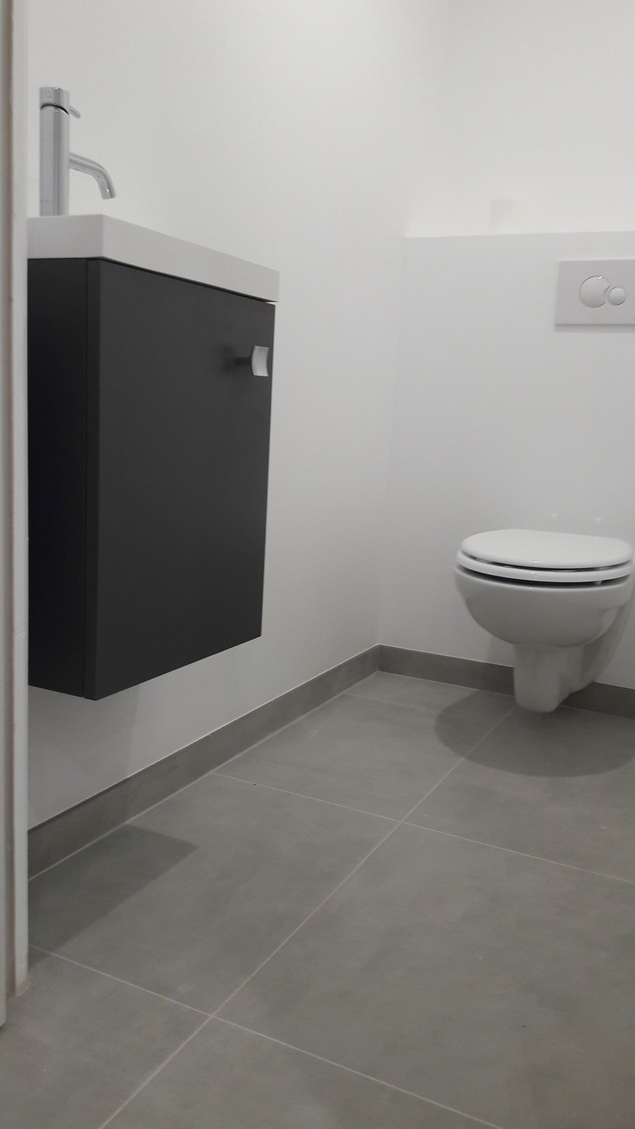 Petite salle de bains moderne avec meuble-lavabo gris foncé, toilettes et sol carrelé gris. Murs blancs.