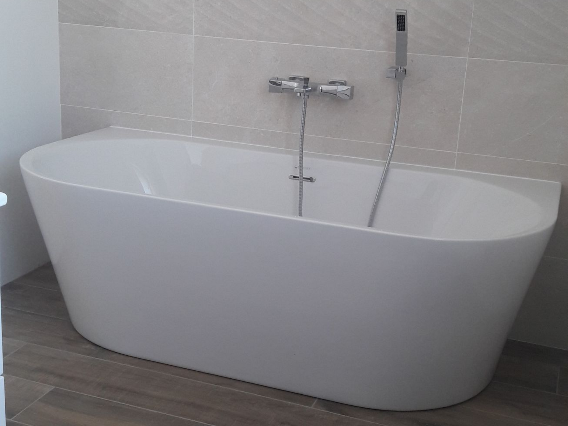 Baignoire en îlot blanche dans une salle de bains, avec robinetterie chromée et mur carrelé de couleur claire.