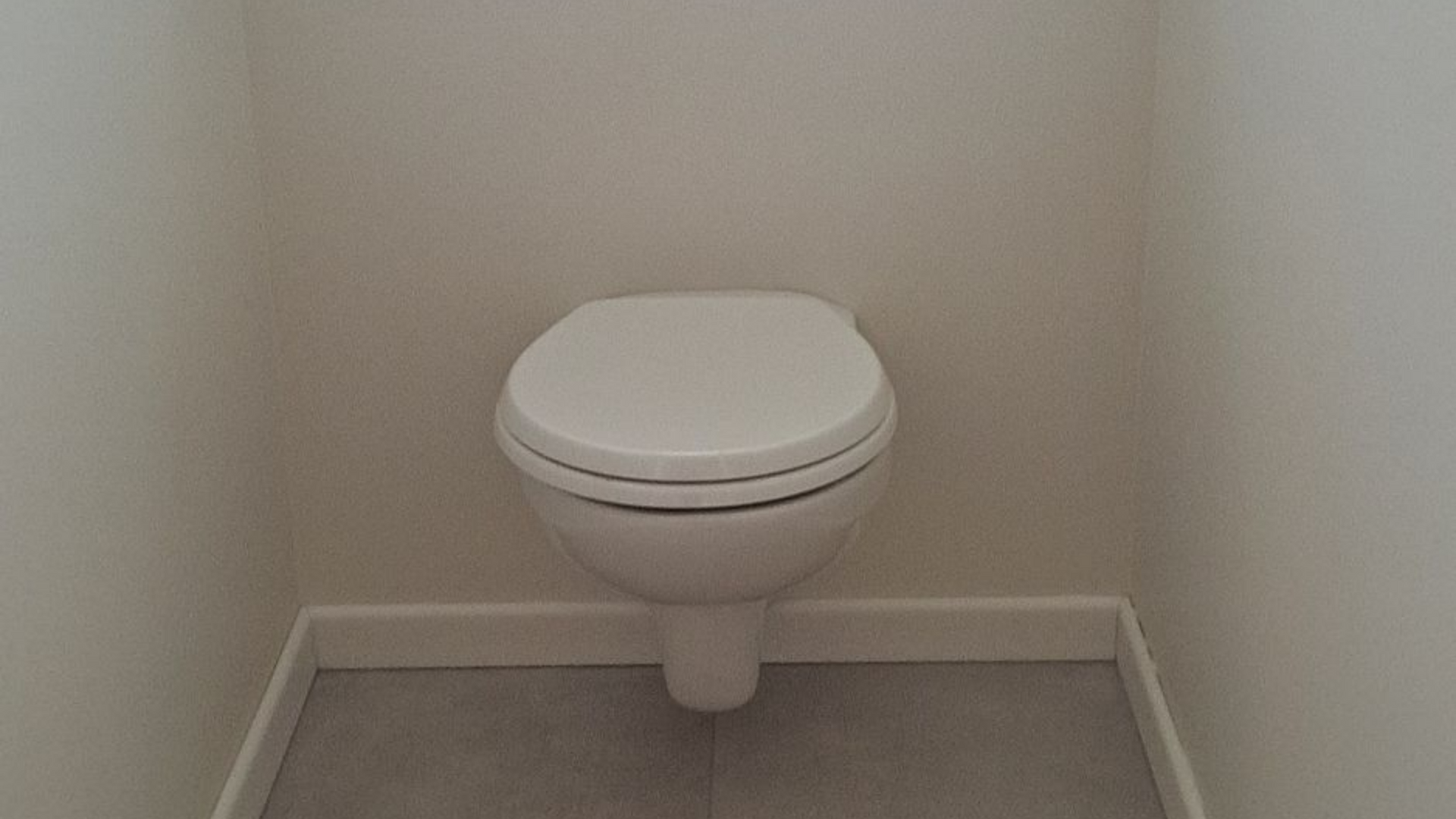 Toilettes blanches dans une petite alcôve avec sol carrelé gris et murs blancs.