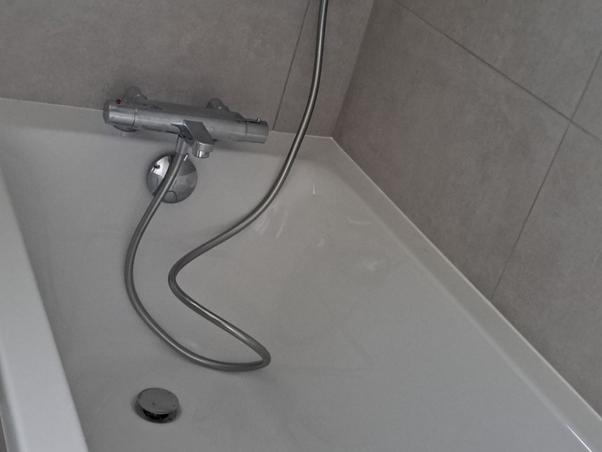 Baignoire blanche avec robinetterie argentée sur un mur carrelé gris.