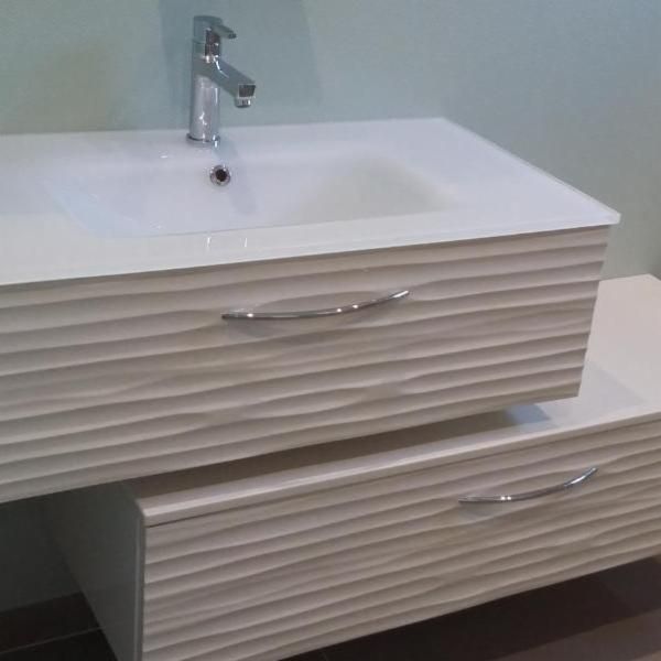 Meuble-lavabo blanc avec deux tiroirs et un lavabo, robinet chromé et façades de tiroirs ondulées.