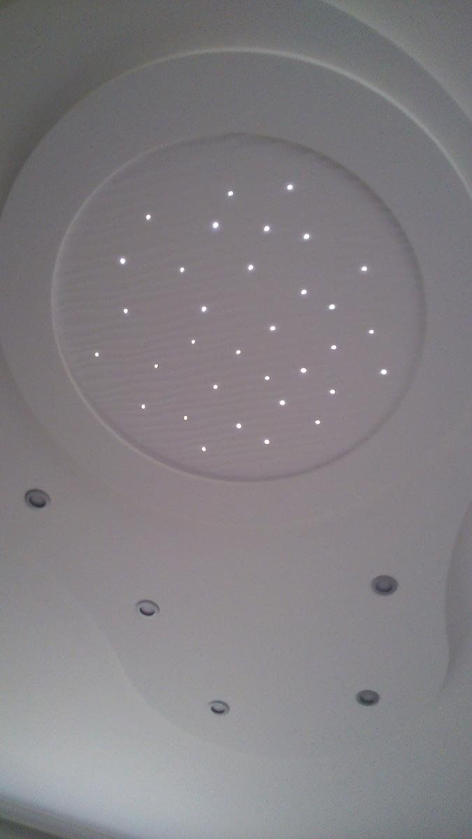 Plafond blanc avec une section circulaire en retrait contenant des lumières en forme d'étoile, entourée d'autres lumières encastrées.