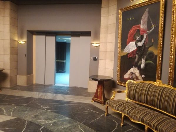 Pasillo con ascensor, pintura ornamentada, muebles dorados y suelo de mármol.