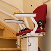 Silla salvaescaleras con asiento rojo y reposabrazos blancos, instalada en una escalera.