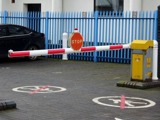 Una barrera de estacionamiento con rayas rojas y blancas y una señal de alto. Valla azul al fondo.
