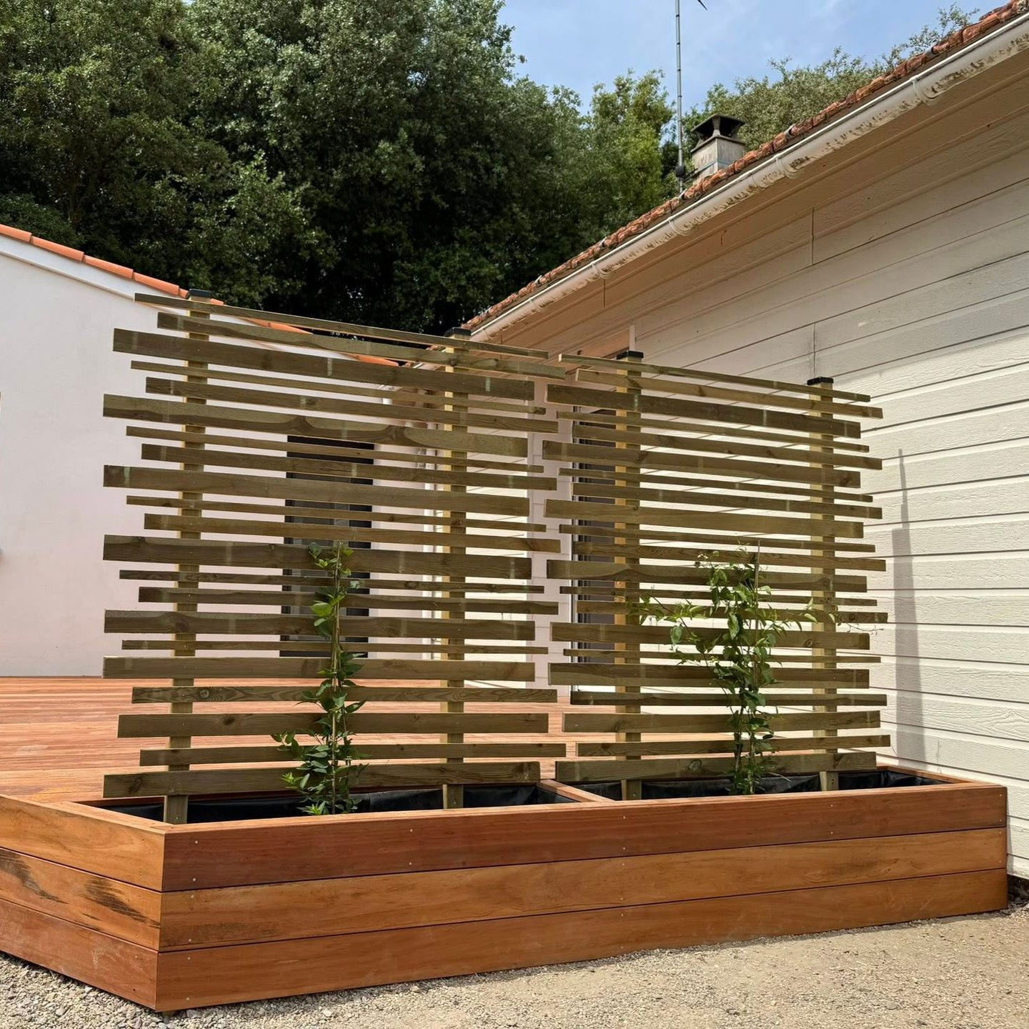 Terrasse en bois avec jardinière intégrée et treillis horizontal devant une maison.