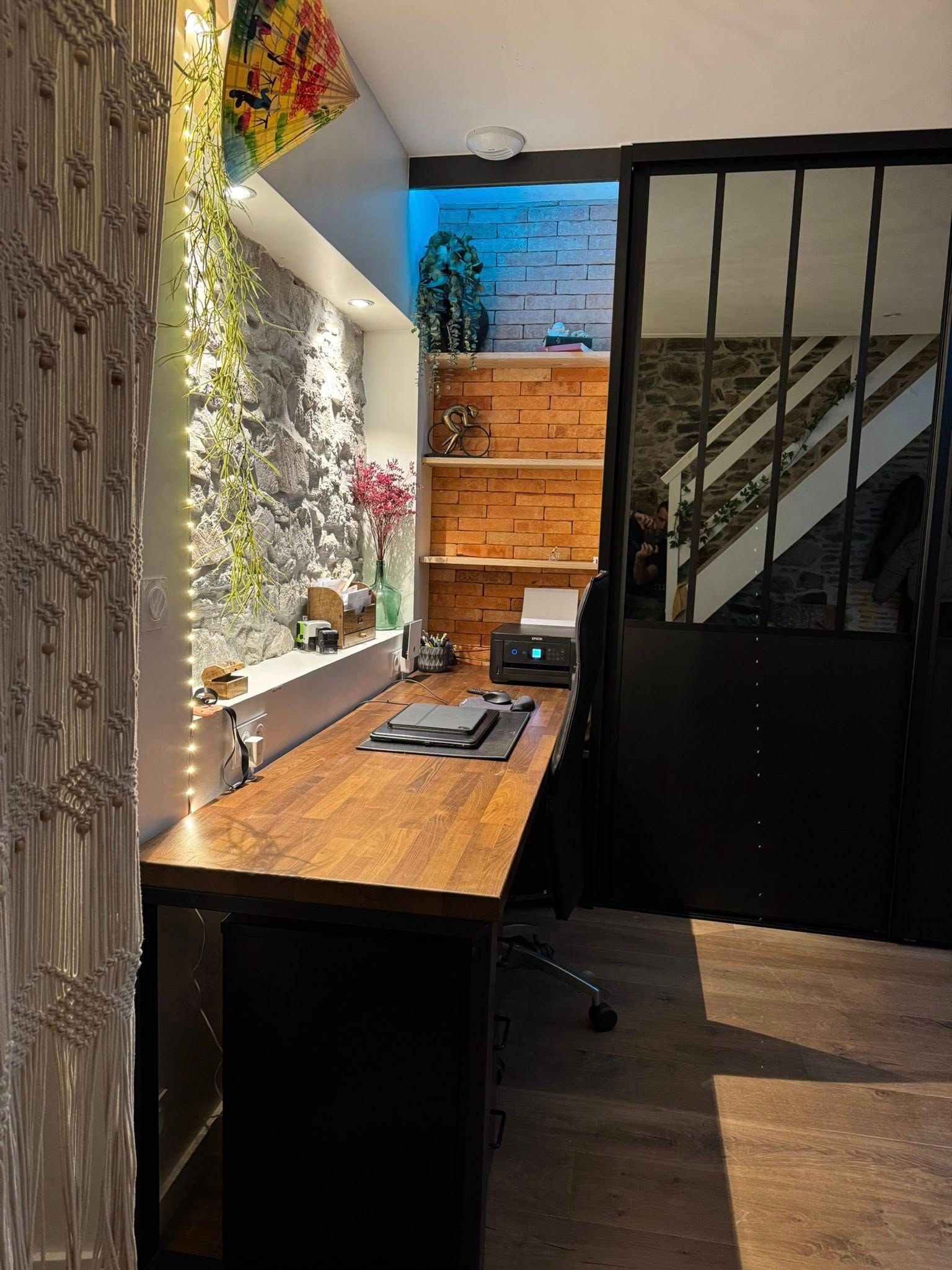 Bureau à domicile avec un bureau en bois, des étagères, un mur en briques et une porte à cadre métallique.