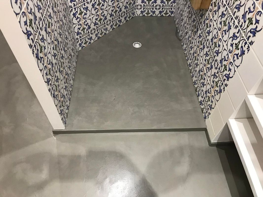 Cabine de douche avec sol en béton gris, murs carrelés de carreaux bleus à motifs et finitions blanches.