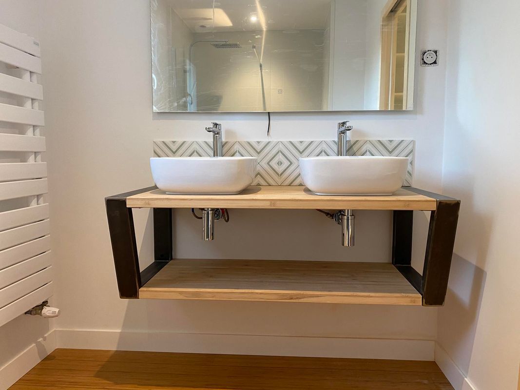 Salle de bains moderne avec meuble-lavabo, double vasque, supports en bois et métal noir. Lavabos blancs et crédence carrelée.