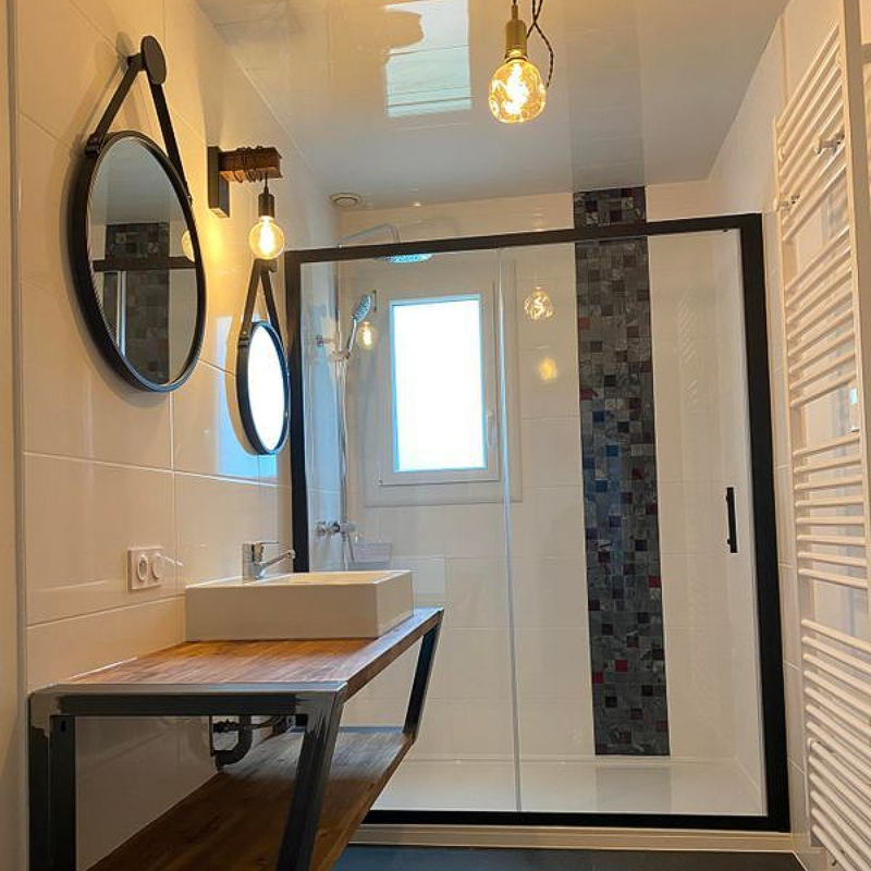 Salle de bains moderne avec douche en verre, meuble-lavabo avec comptoir en bois et éclairage décoratif.