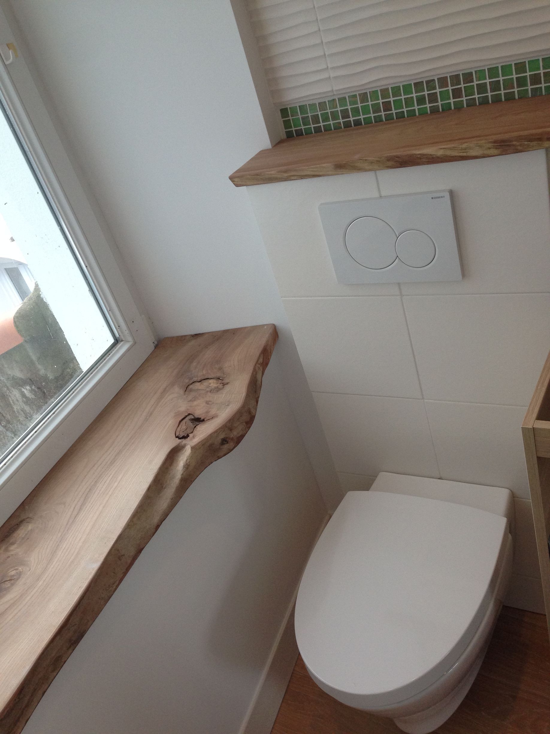 Salle de bains avec toilettes blanches, étagères en bois et fenêtre.