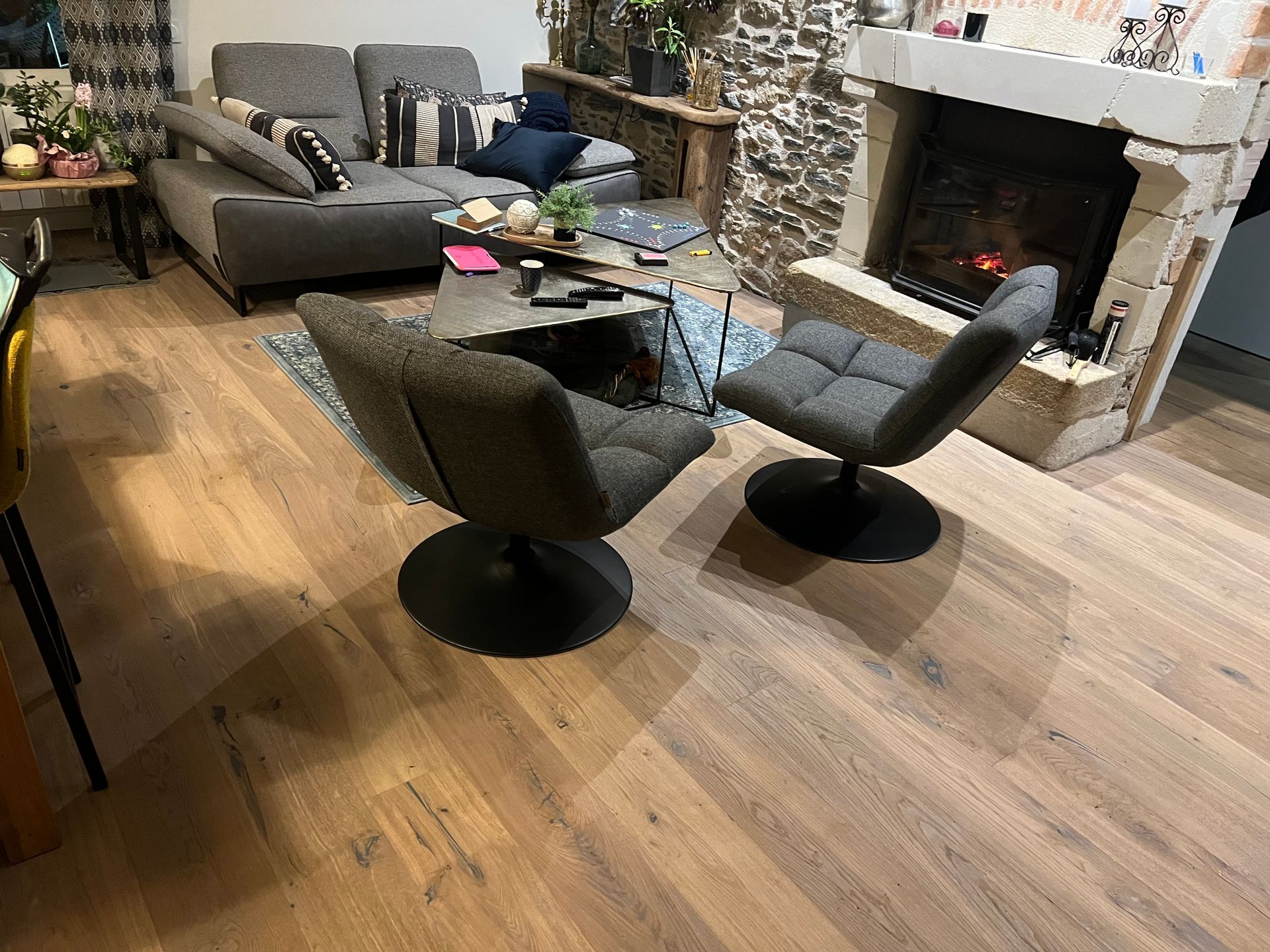 Salon avec canapé gris, fauteuils pivotants, cheminée et parquet.