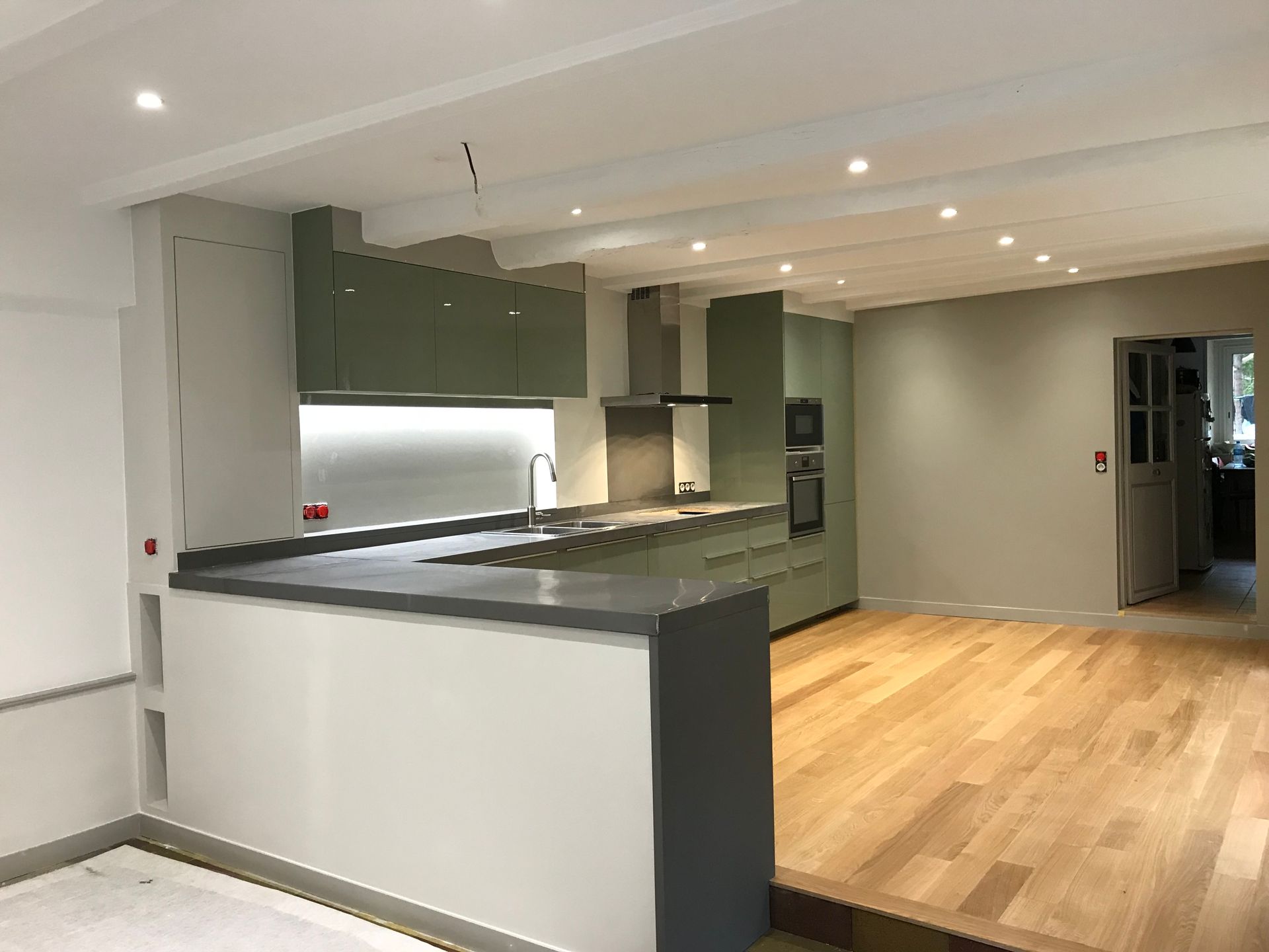 Cuisine moderne avec placards vert sauge, plans de travail gris et parquet.