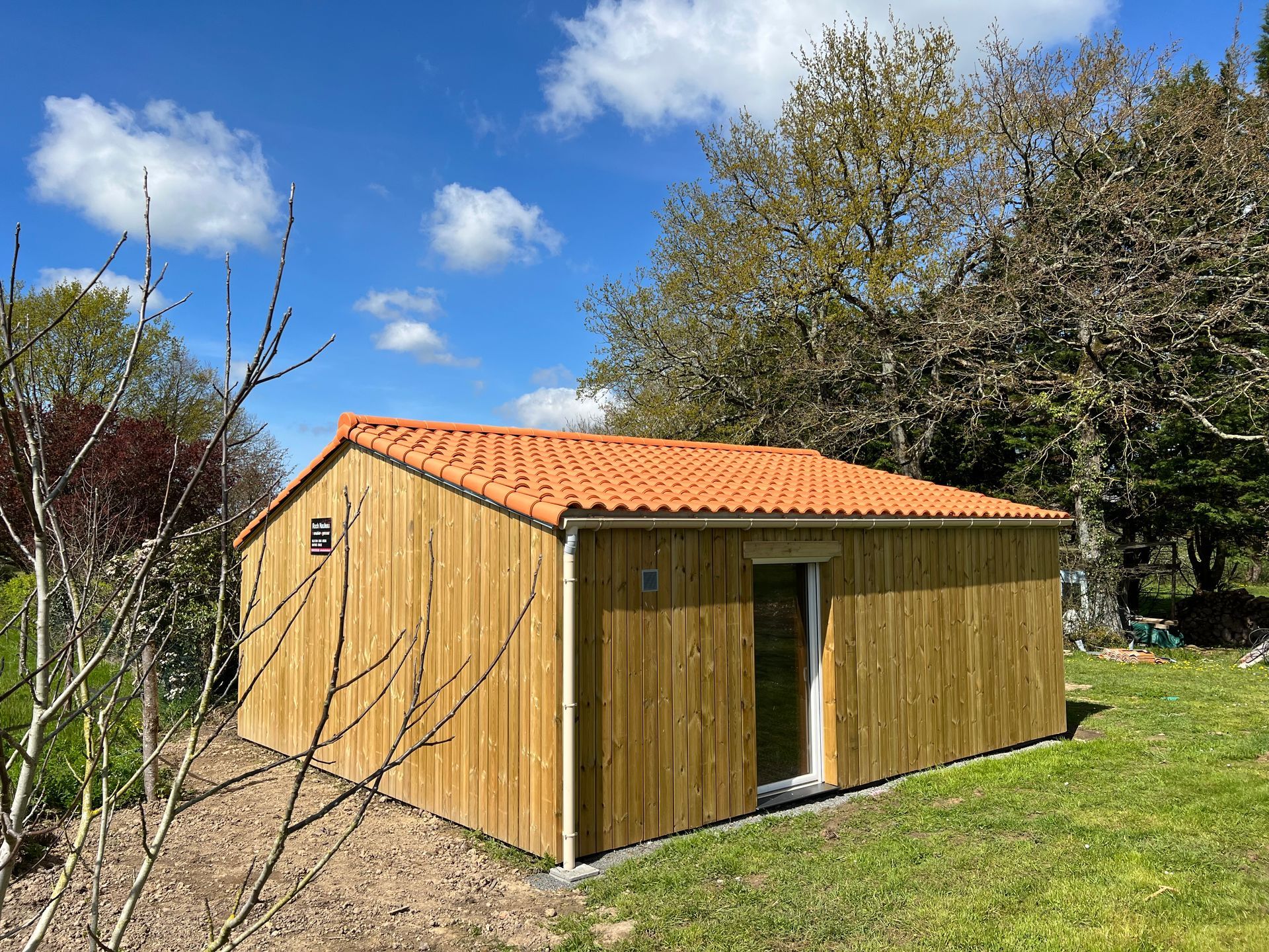 Cabane en bois au toit de tuiles orange sur une pelouse sous un ciel bleu.
