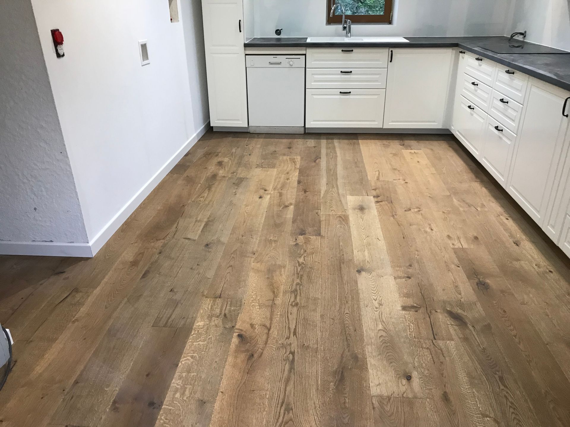 Sol en bois dans une cuisine avec placards, plans de travail et appareils électroménagers blancs.