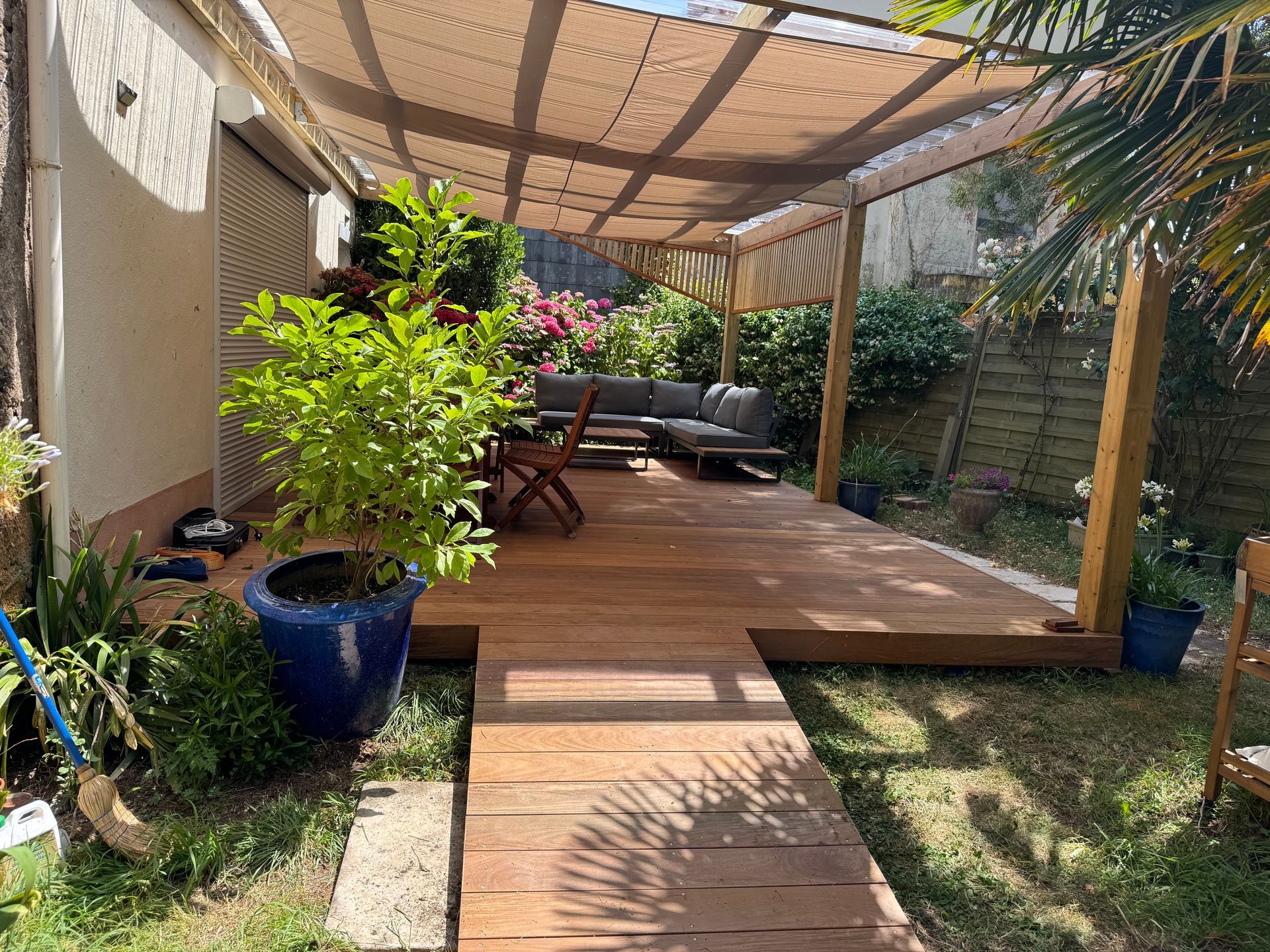 Terrasse en bois avec pergola, sièges extérieurs et végétation luxuriante dans un jardin.