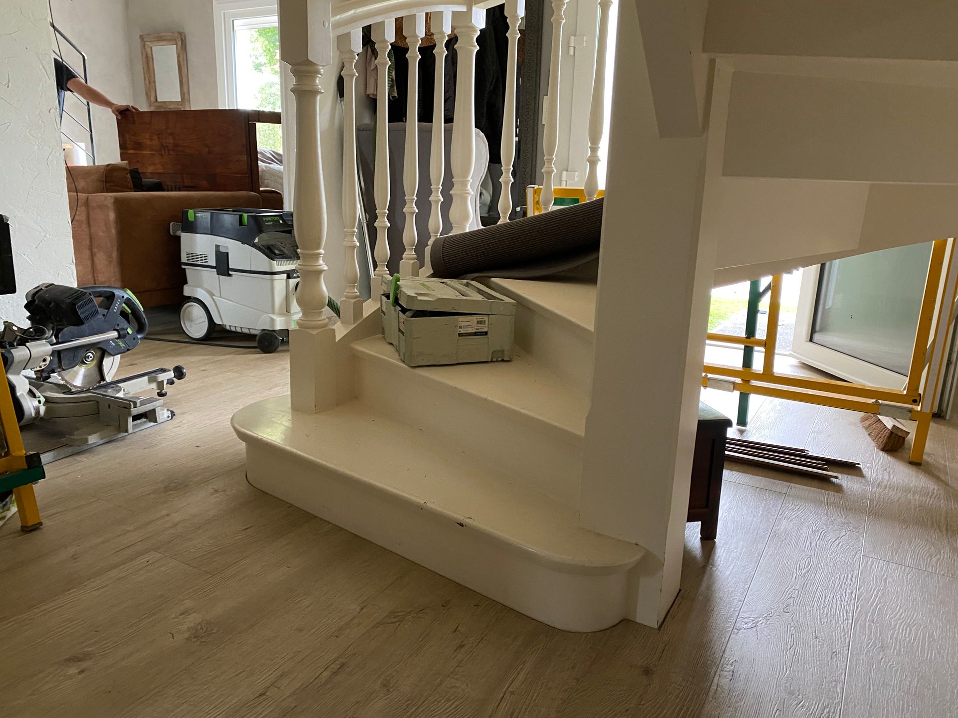 Un escalier peint en blanc avec des outils, un parquet et une personne debout à proximité.
