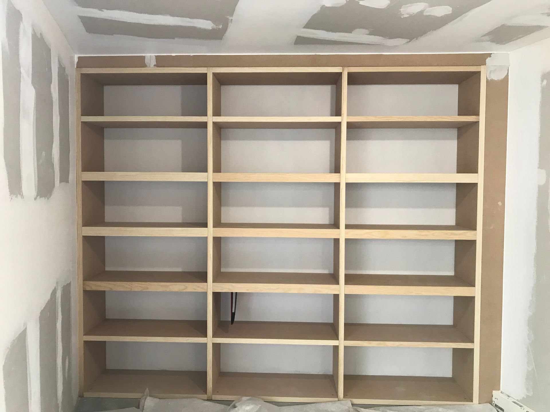 Bibliothèque en bois encastrée dans un mur lors de la construction, entourée de plaques de plâtre non finies.