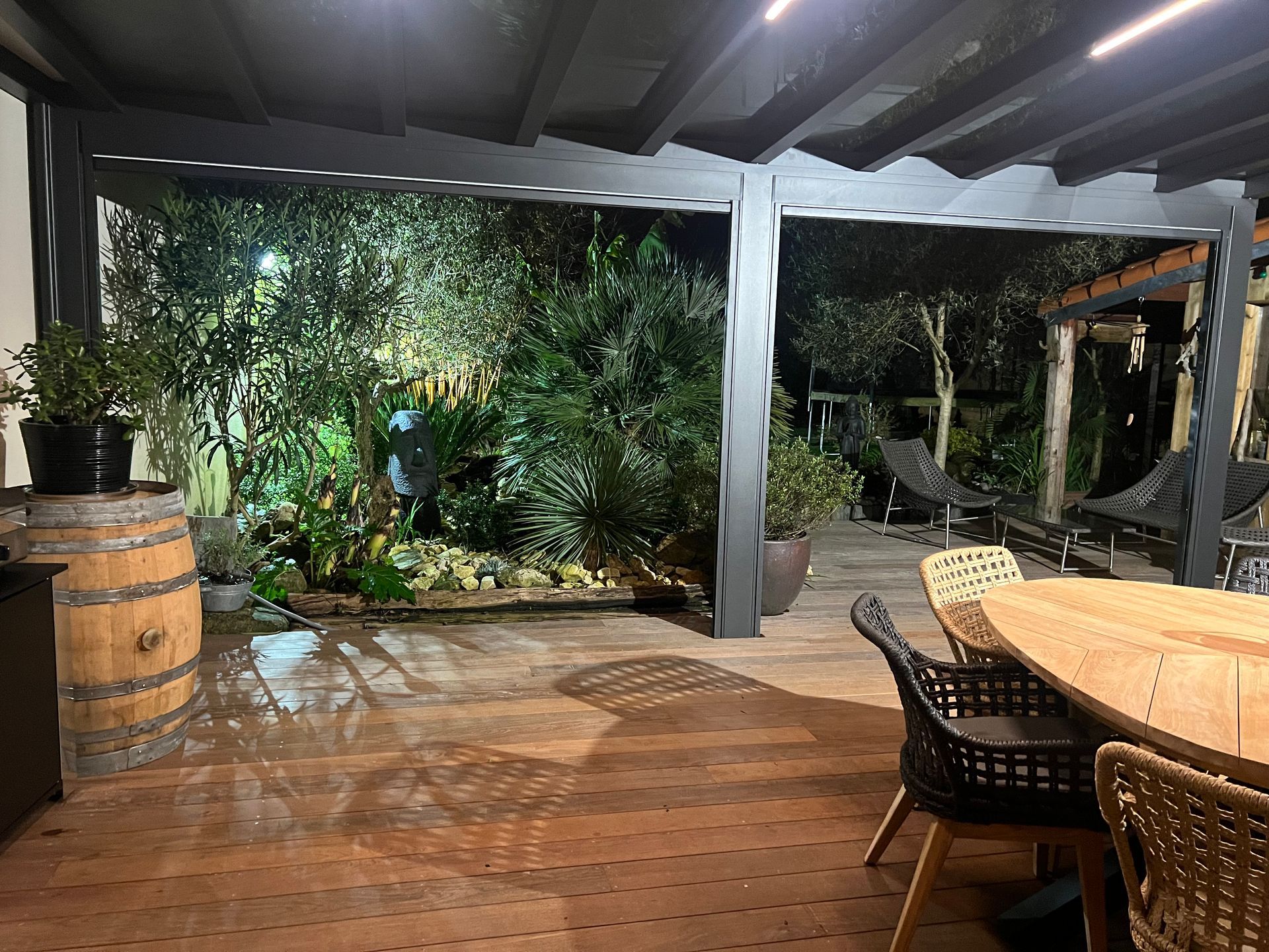 Terrasse en bois avec table à manger extérieure et jardin la nuit.