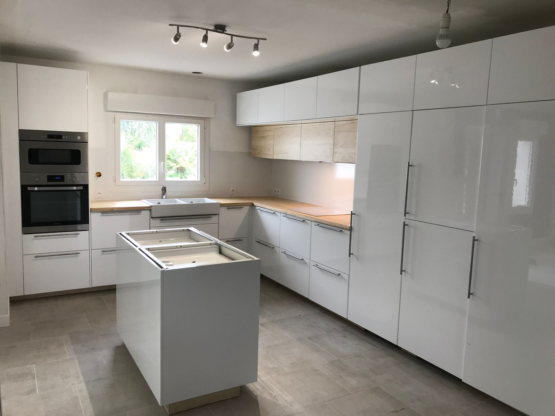 Cuisine moderne blanche avec armoires laquées, comptoirs en bois, îlot et électroménagers en acier inoxydable.