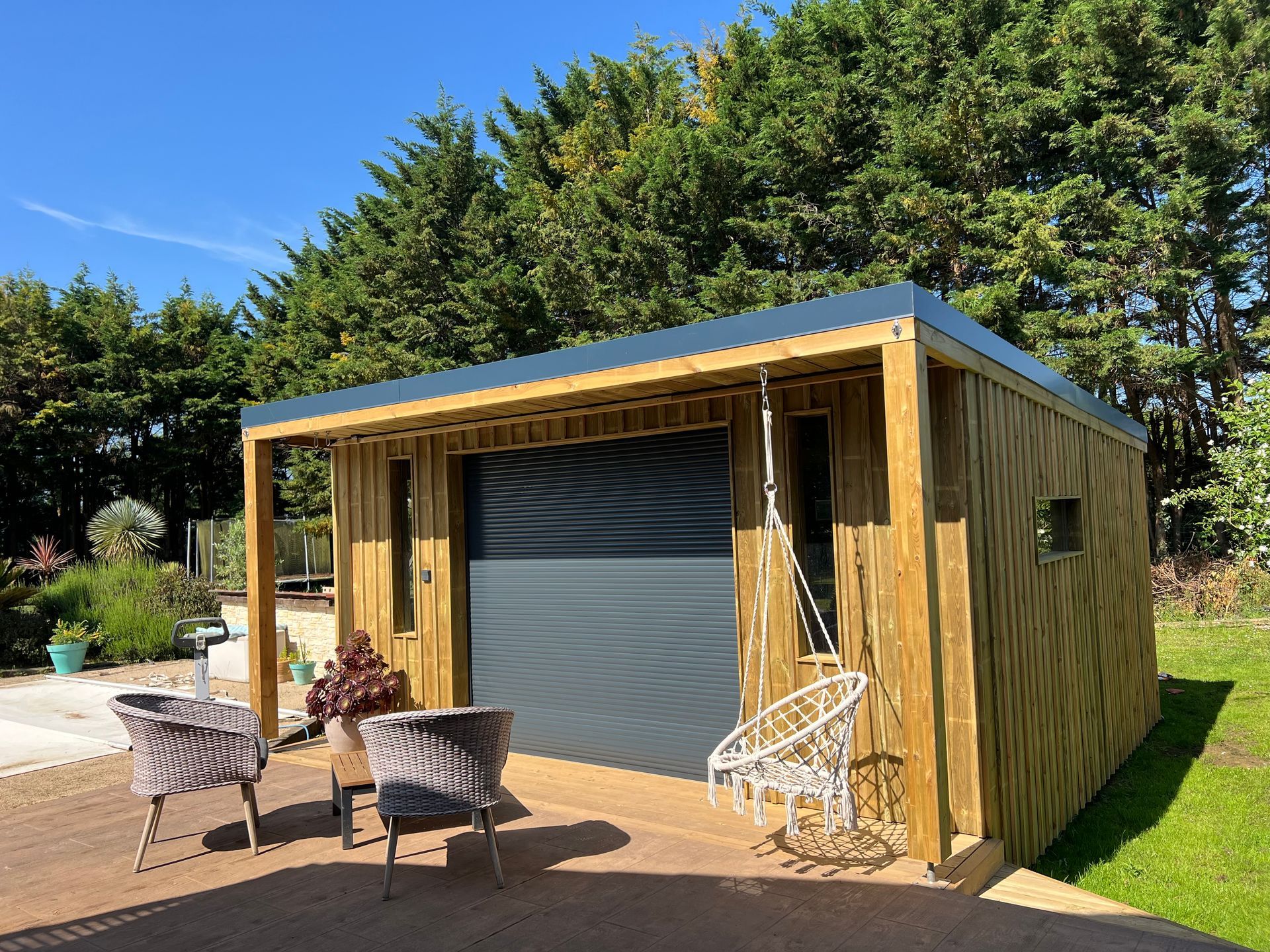 Un chemin de bois mène à une entrée sombre, bordée de buissons verts. Cadre extérieur ensoleillé.