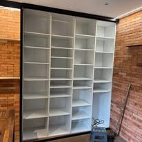 Étagère encastrée blanche et vide, comportant plusieurs compartiments, adossée à un mur de briques.
