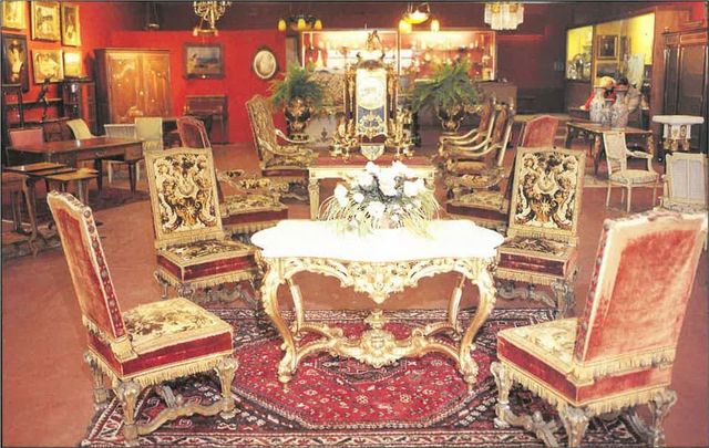 Meubles anciens richement décorés dans un showroom aux murs rouges ; touches dorées, tapis rouges et œuvres d'art.