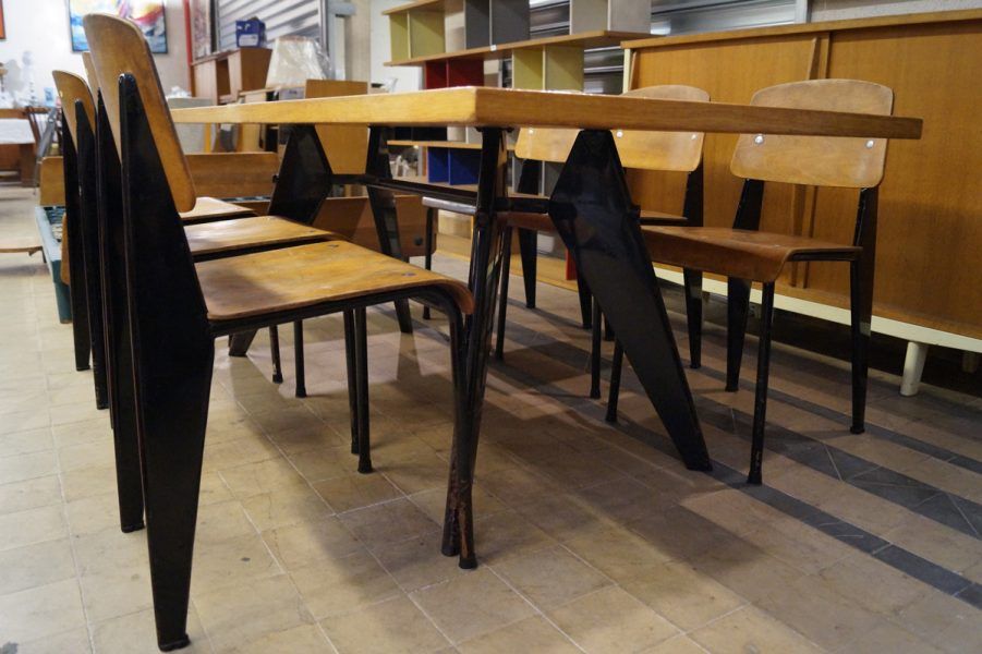 Table à manger avec pieds en métal noir, chaises et plateau en bois dans un espace intérieur.