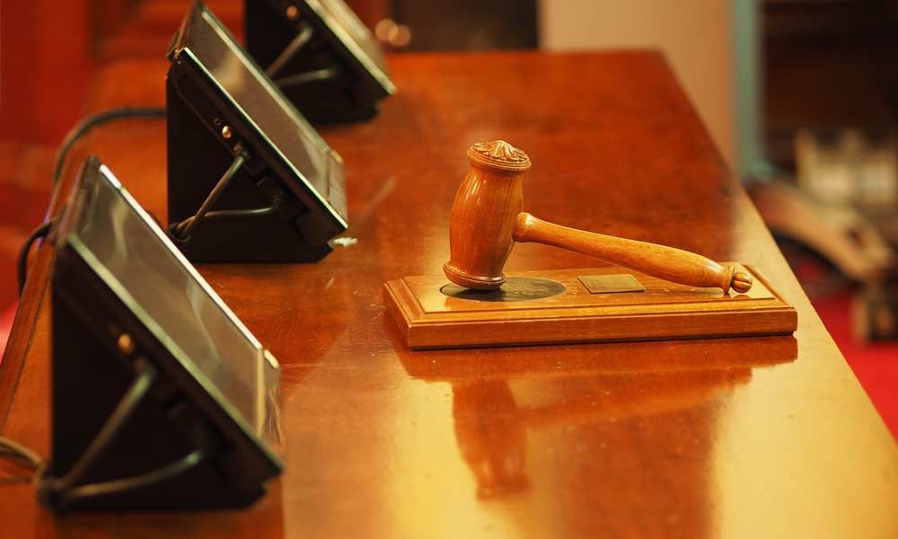 Un maillet en bois posé sur un support, lui-même placé sur une surface en bois brun brillant, avec trois écrans inclinés au premier plan.