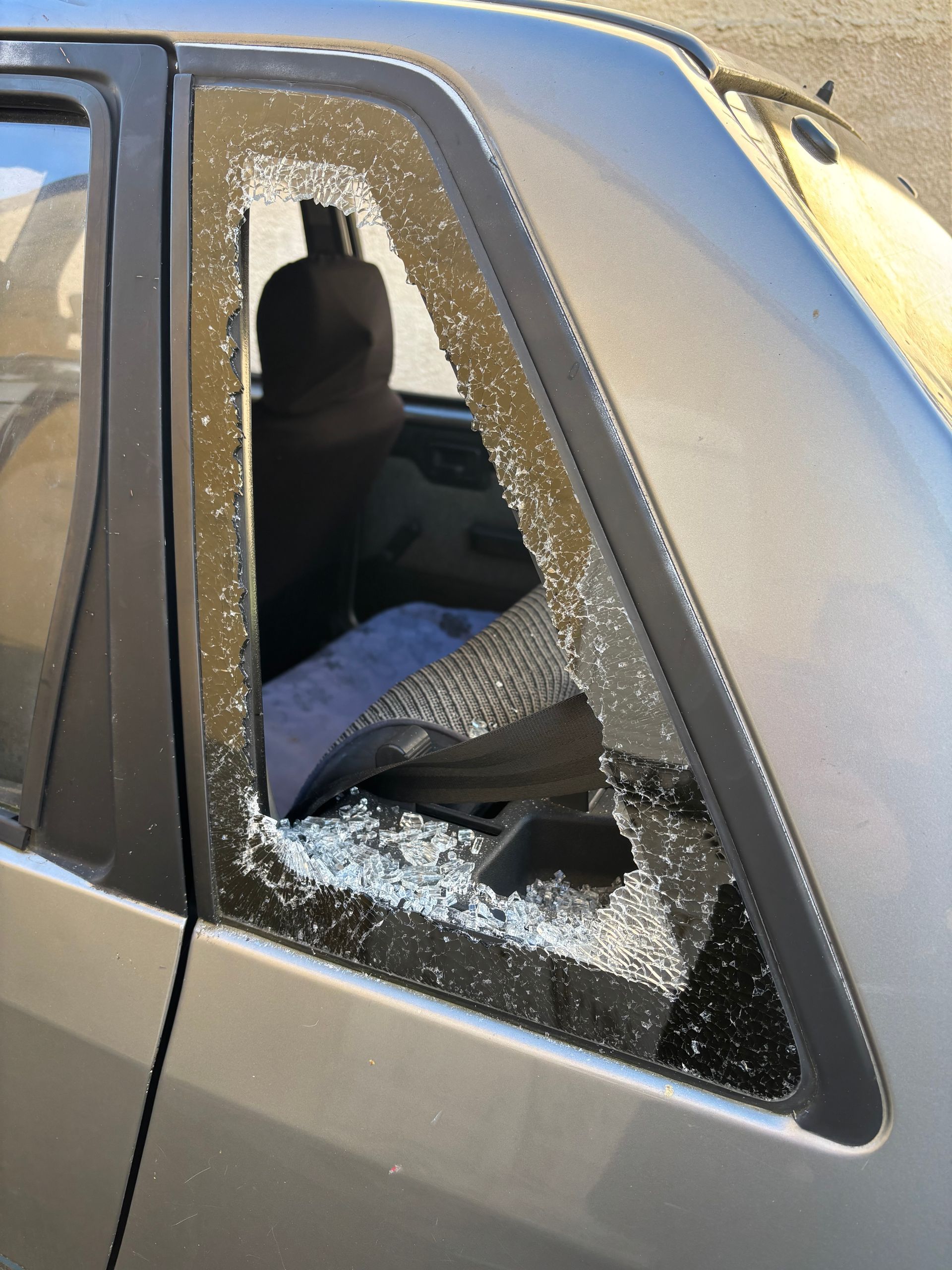 Une vitre de custode brisée sur le côté d'une voiture argentée, avec des éclats de verre recouvrant l'intérieur arrière.