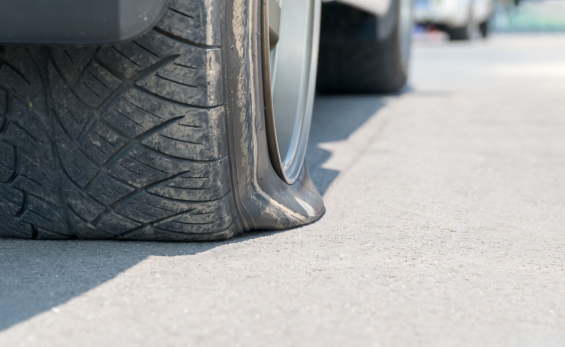 Gros plan sur un pneu de voiture complètement dégonflé, reposant sur sa jante métallique sur une route goudronnée.