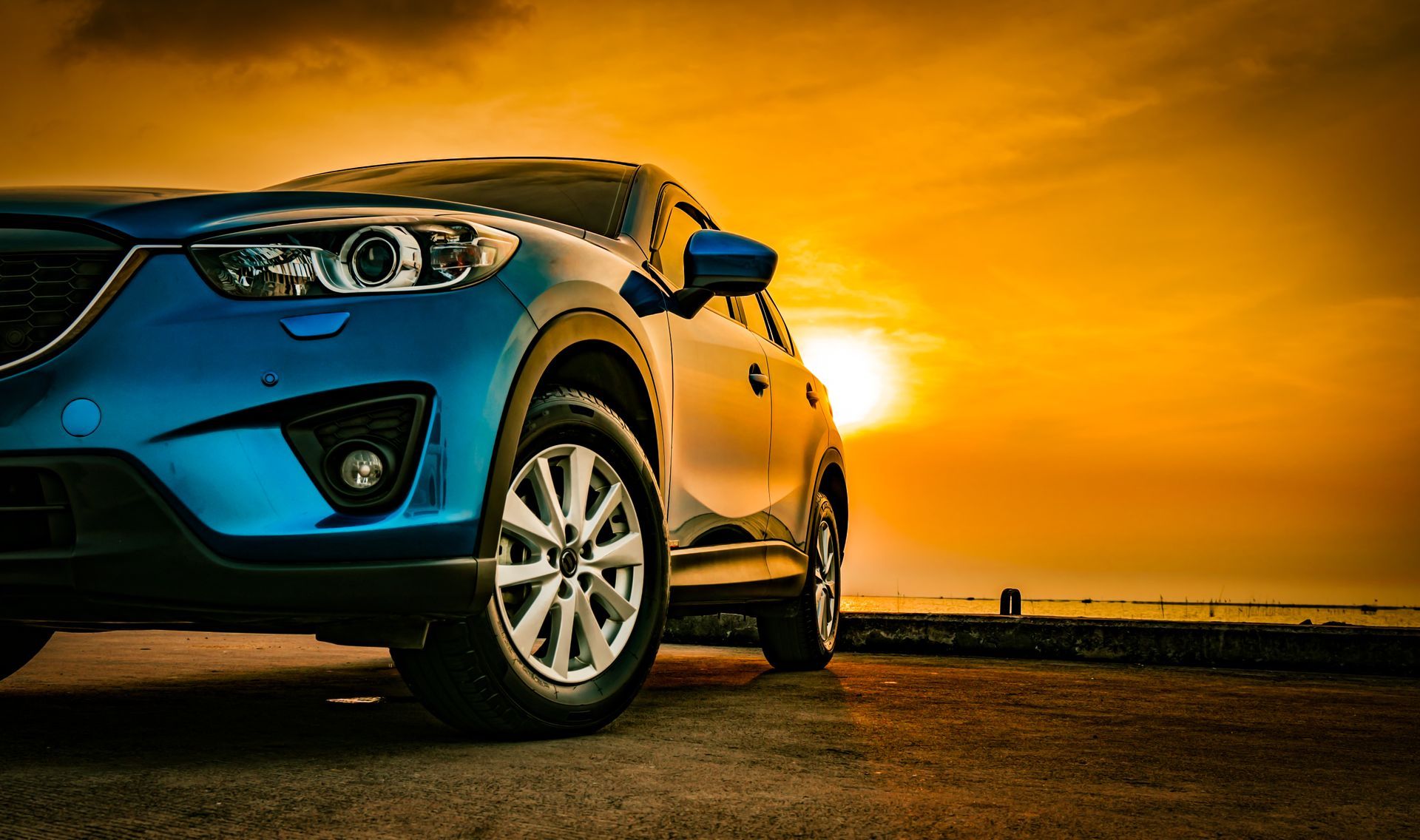 Un SUV bleu garé devant un magnifique coucher de soleil doré au bord de l'eau.