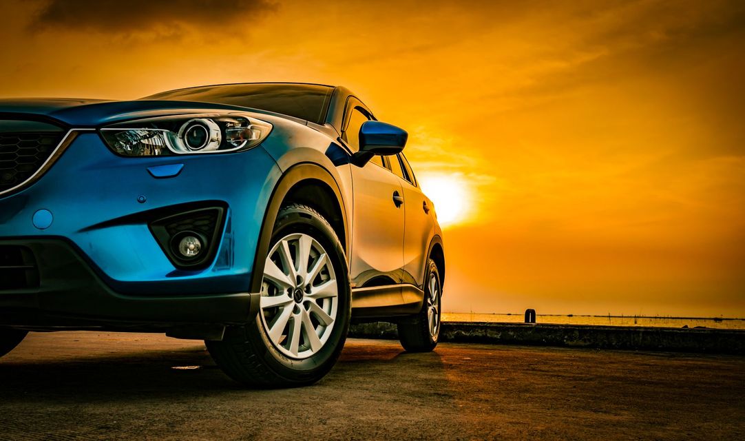 Un SUV bleu garé devant un magnifique coucher de soleil doré au bord de l'eau.