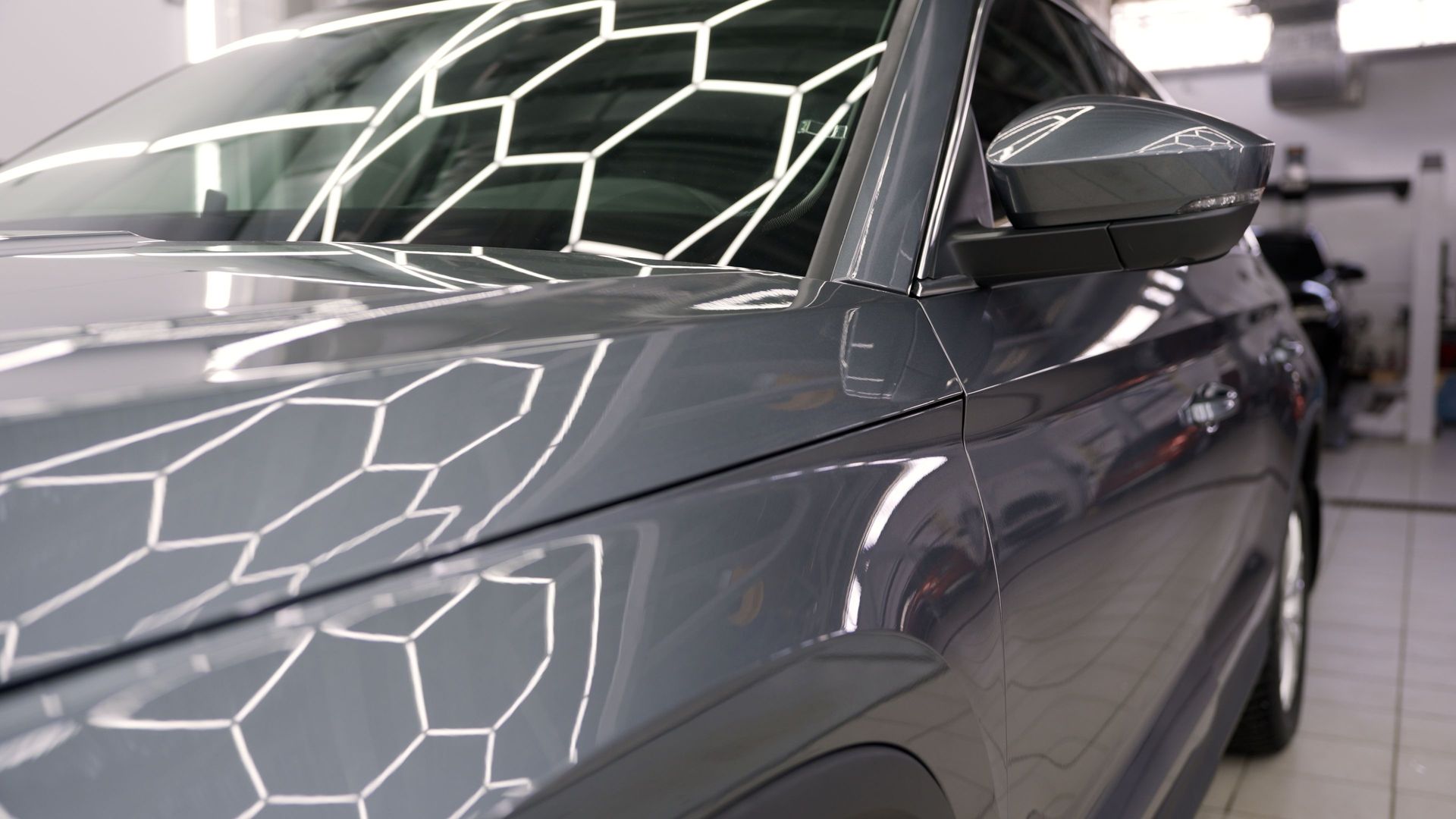 Gros plan en biais du capot et de la portière latérale gris foncé brillant d'une voiture, reflétant les lumières géométriques d'un magasin.