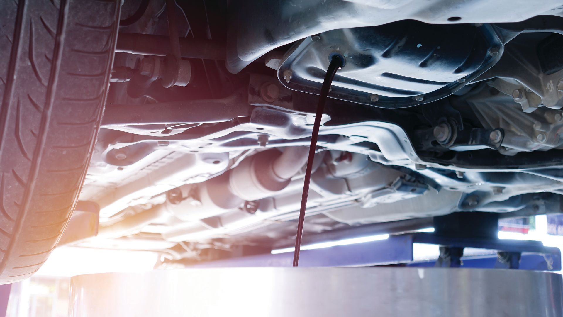 Lors d'une révision, l'huile moteur usagée s'écoule du dessous de la voiture dans un bac de récupération.