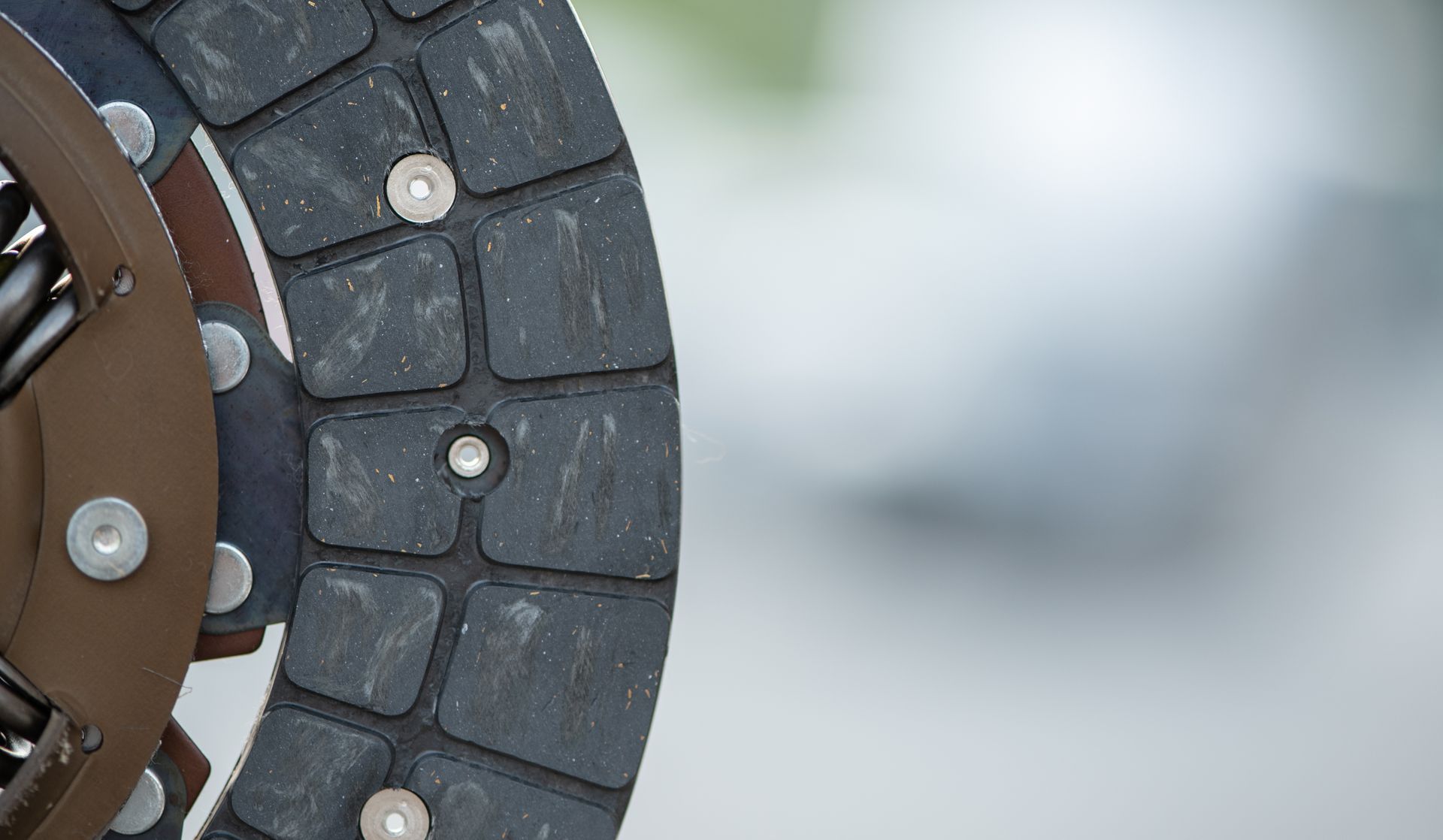 Gros plan sur un disque d'embrayage automobile circulaire avec des segments de friction texturés gris foncé et des rivets métalliques.