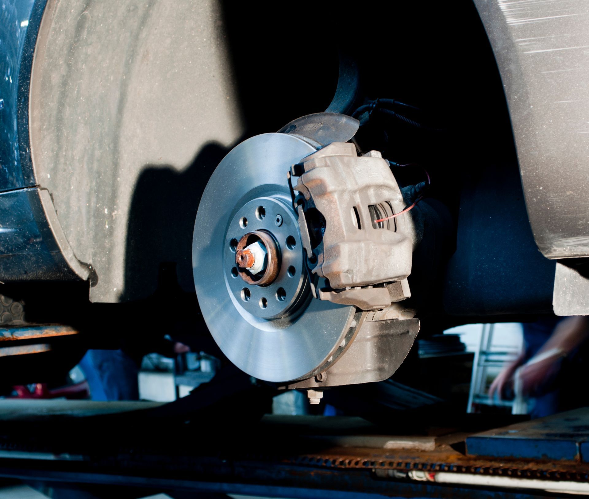 Gros plan sur le système de freins à disque métalliques d'une voiture, monté sur un véhicule surélevé dans un atelier de réparation automobile.
