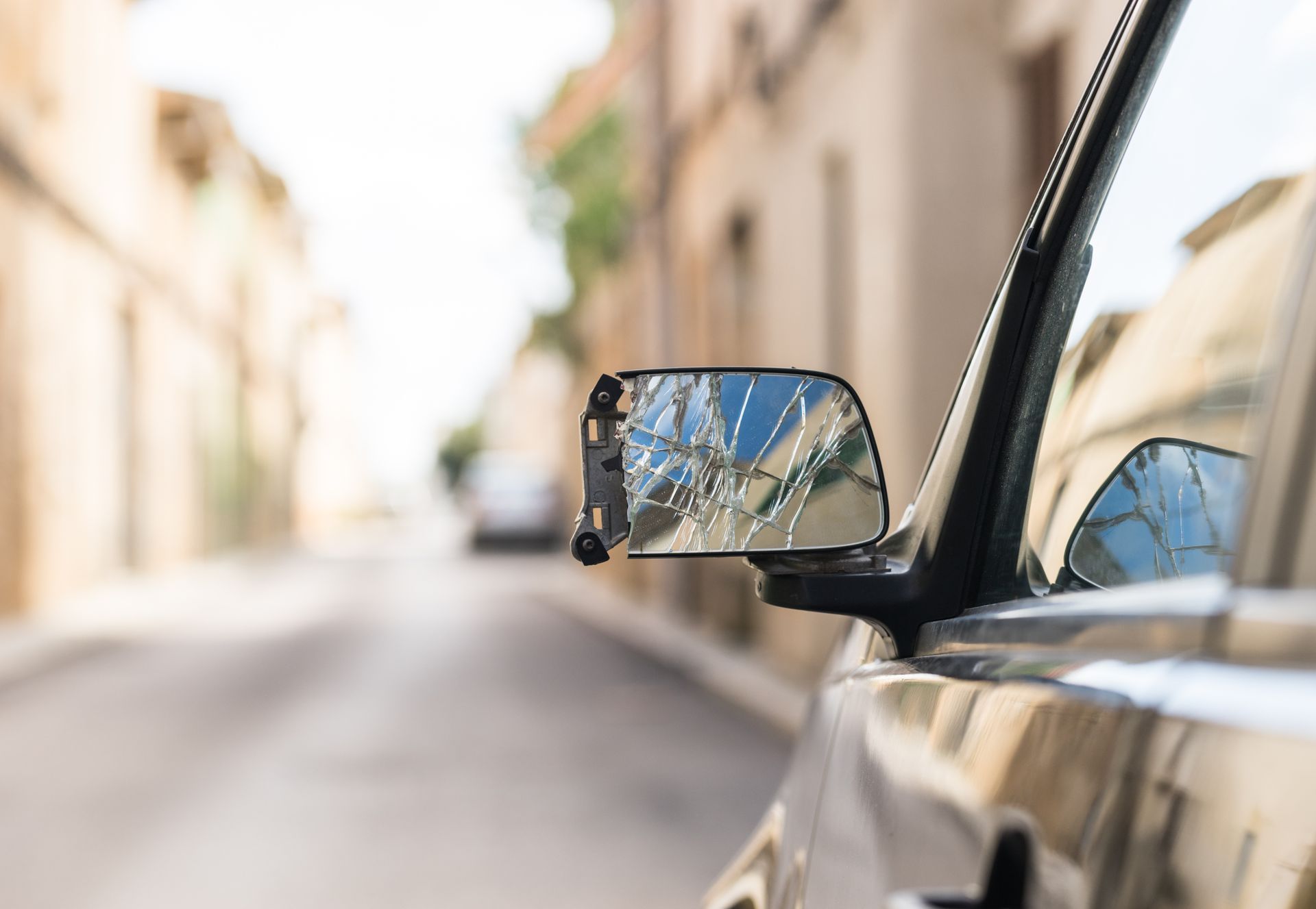 Gros plan sur le rétroviseur d'une voiture reflétant une rue étroite et ensoleillée bordée de bâtiments.