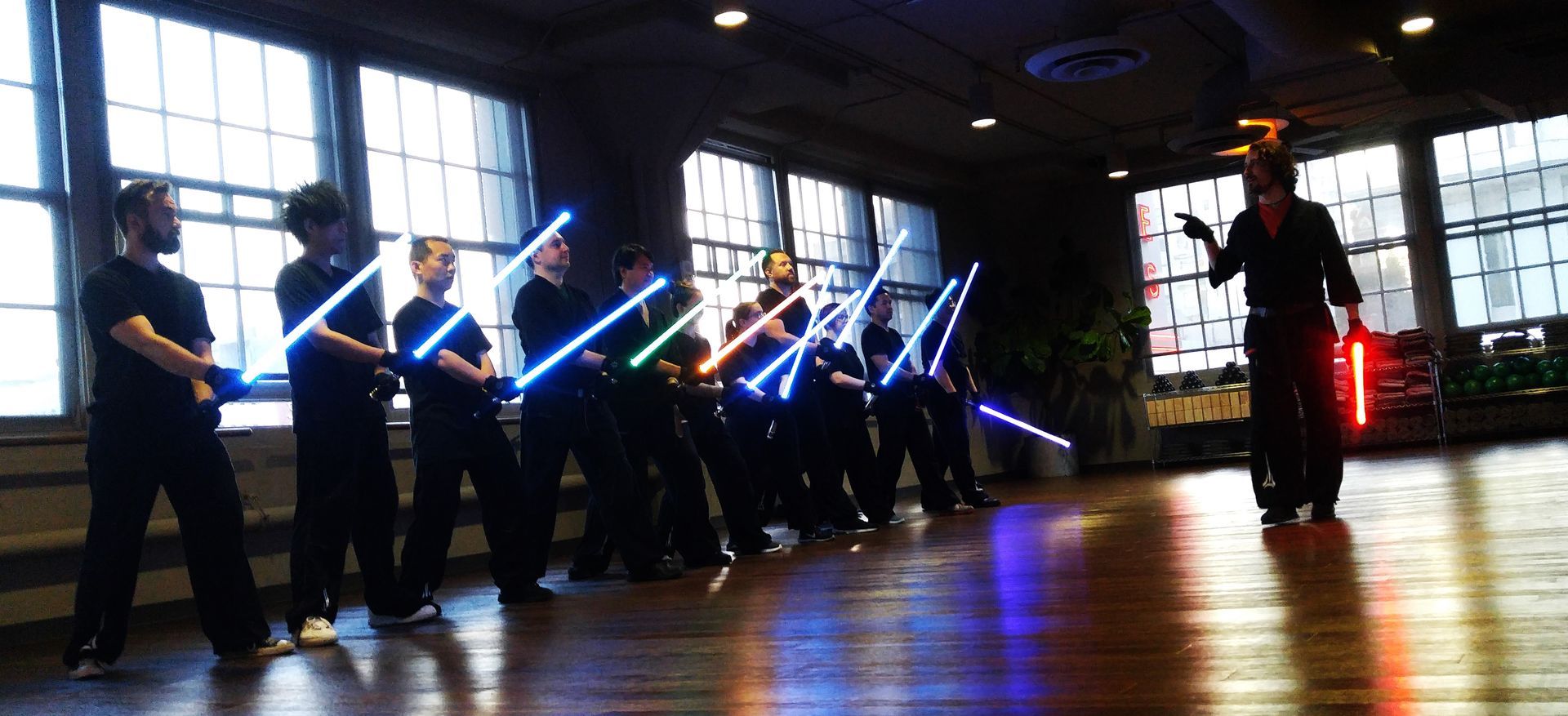 En una sala grande, unas personas con sables de luz se enfrentan a una persona con un sable de luz rojo.