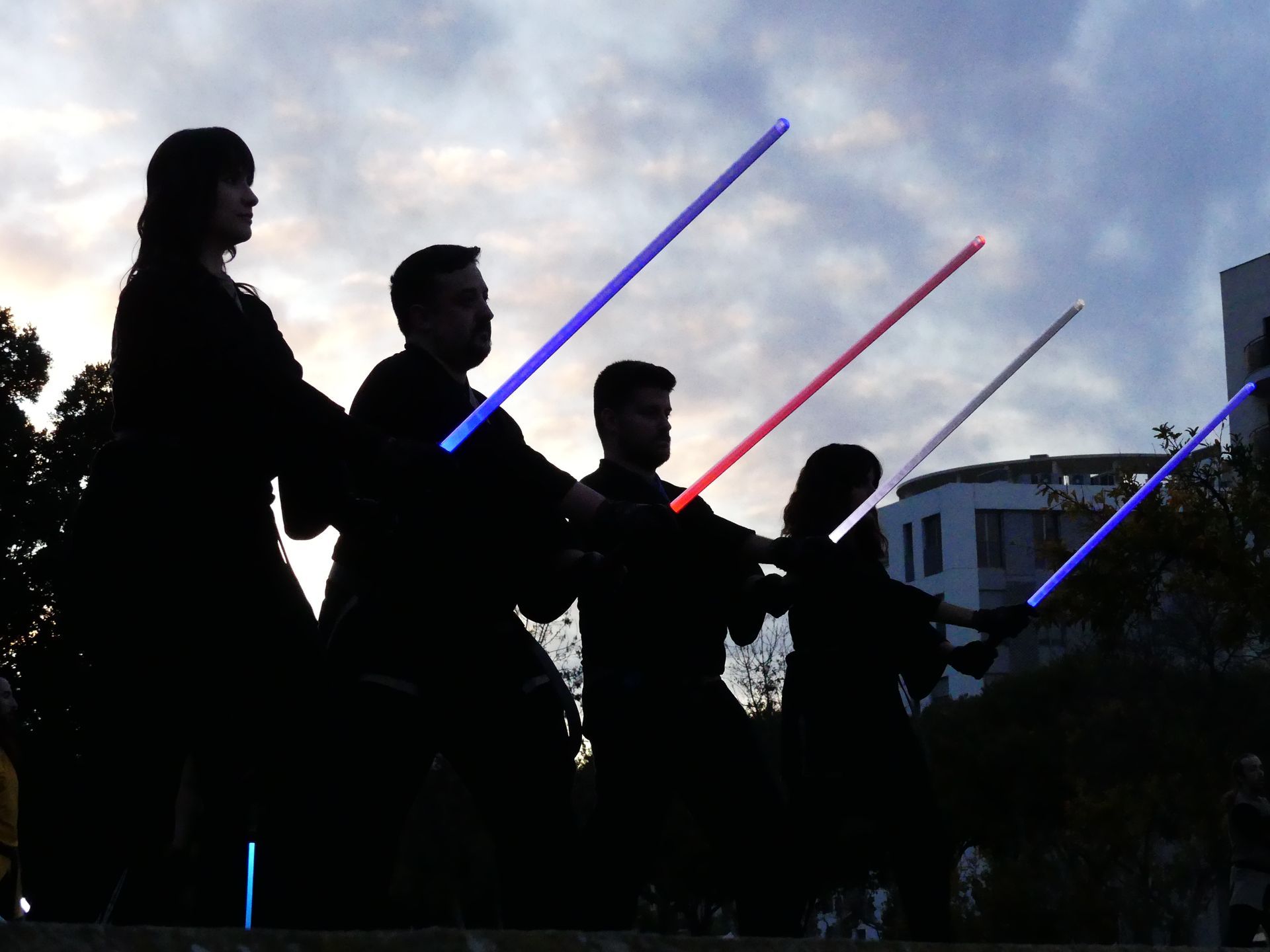 Figuras silueteadas sosteniendo sables de luz encendidos, contra un cielo nublado.