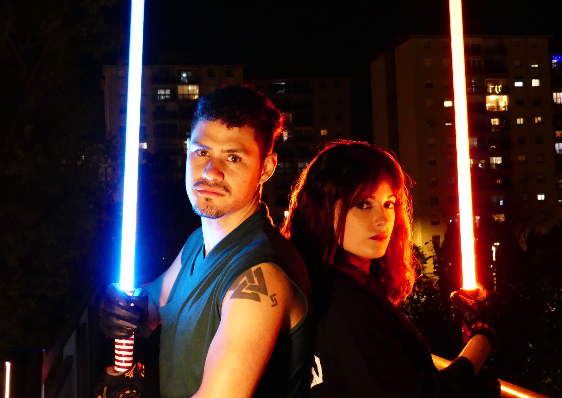 Hombre y mujer con sables de luz. El hombre sostiene un sable azul. La mujer sostiene un sable rojo.