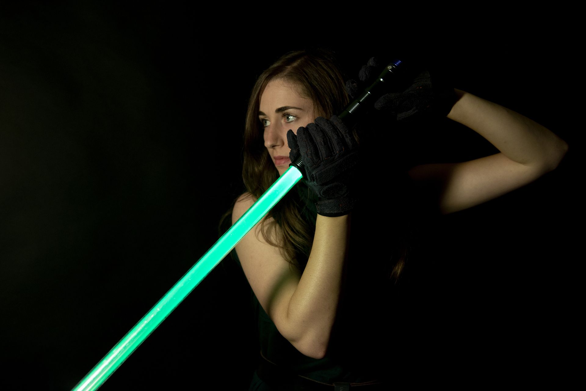 Mujer vestida con ropa oscura, empuñando un sable de luz verde sobre un fondo negro.