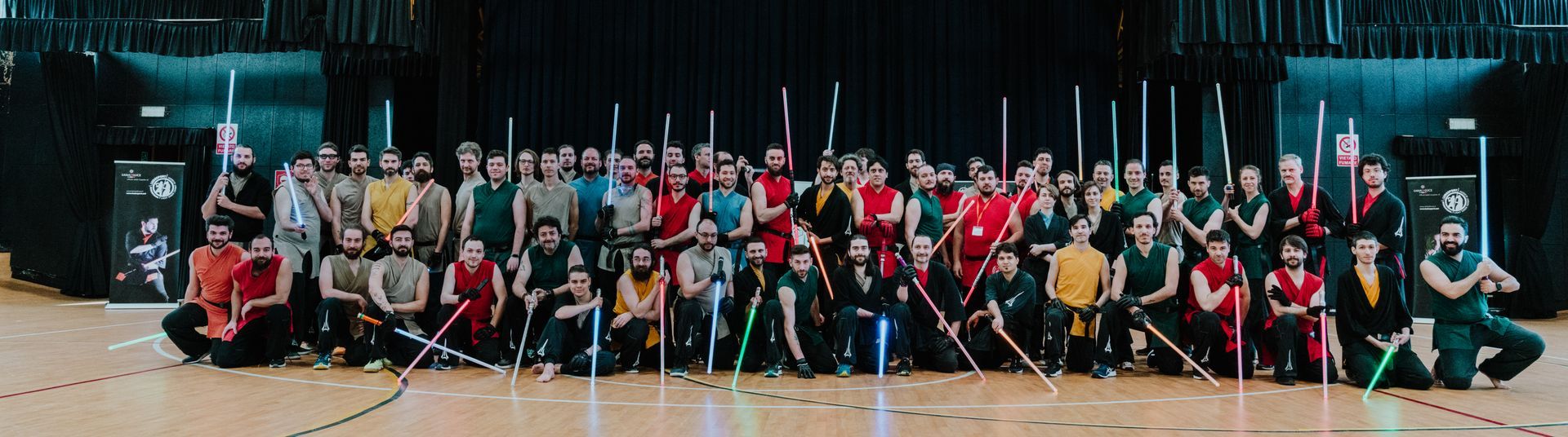 Grupo de personas con sables de luz en un espacio interior, algunos arrodillados, con sables de diferentes colores.