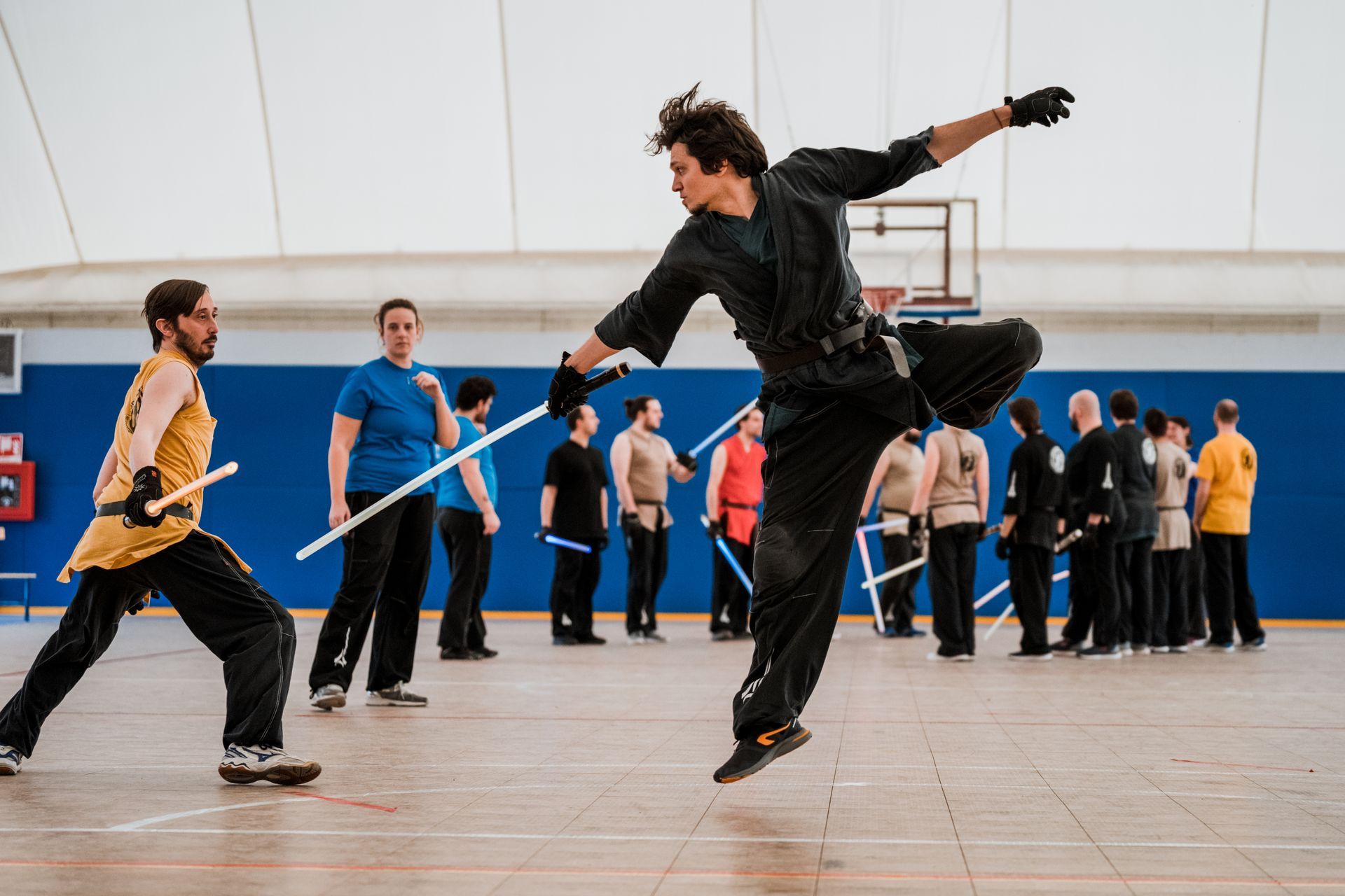 Un hombre vestido de negro salta y se lanza hacia otro hombre que empuña un bastón en el interior, mientras otros lo observan