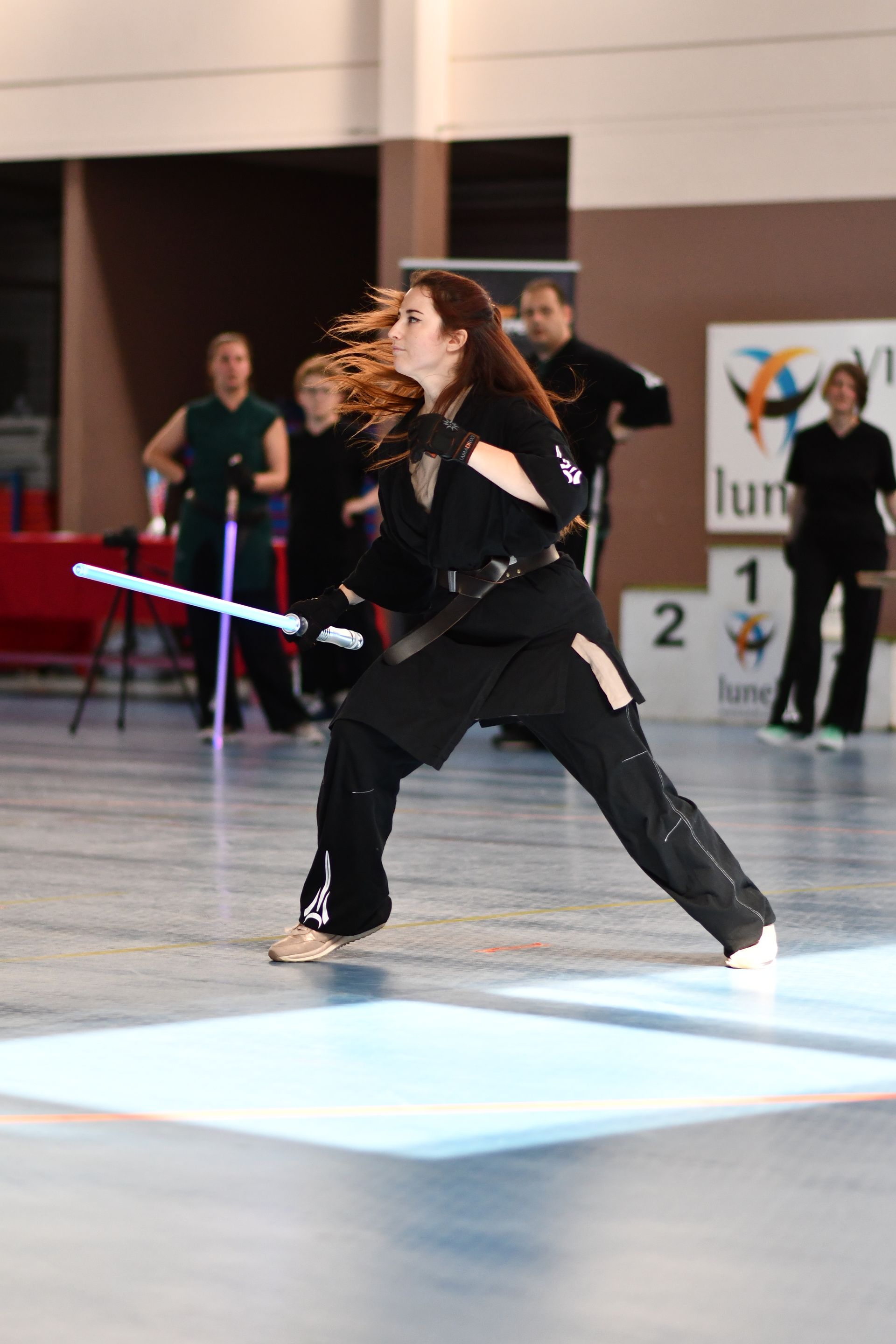 Mujer en traje negro con sable de luz, en pose de combate, en una competición.