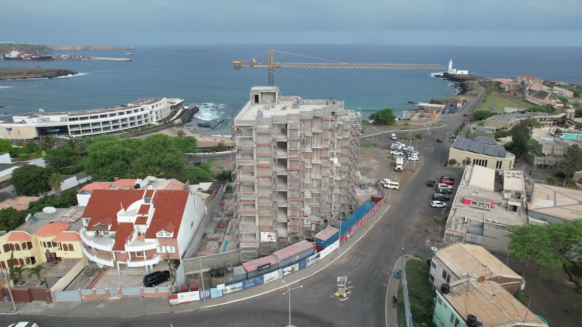 Vista aérea de um edifício parcialmente construído junto ao oceano, com um guindaste e estruturas circundantes.