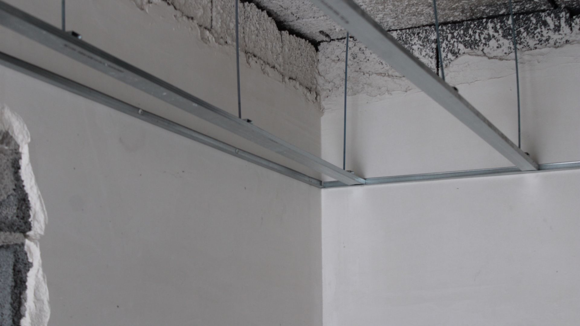 Estrutura metálica para teto rebaixado em sala com paredes brancas.