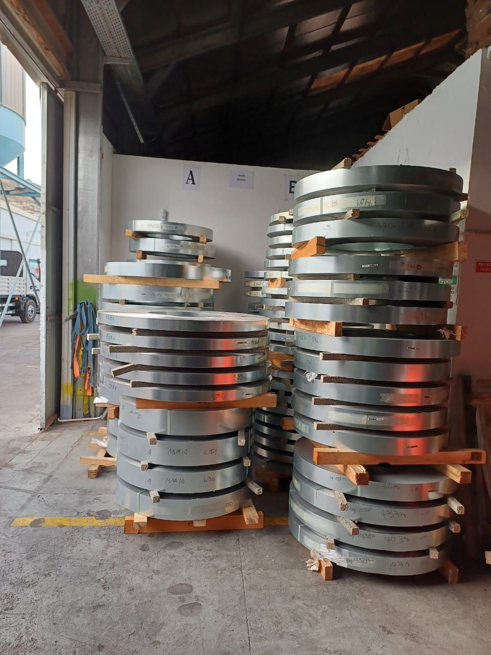 Pilhas de tiras de metal enroladas em paletes de madeira em um armazém.