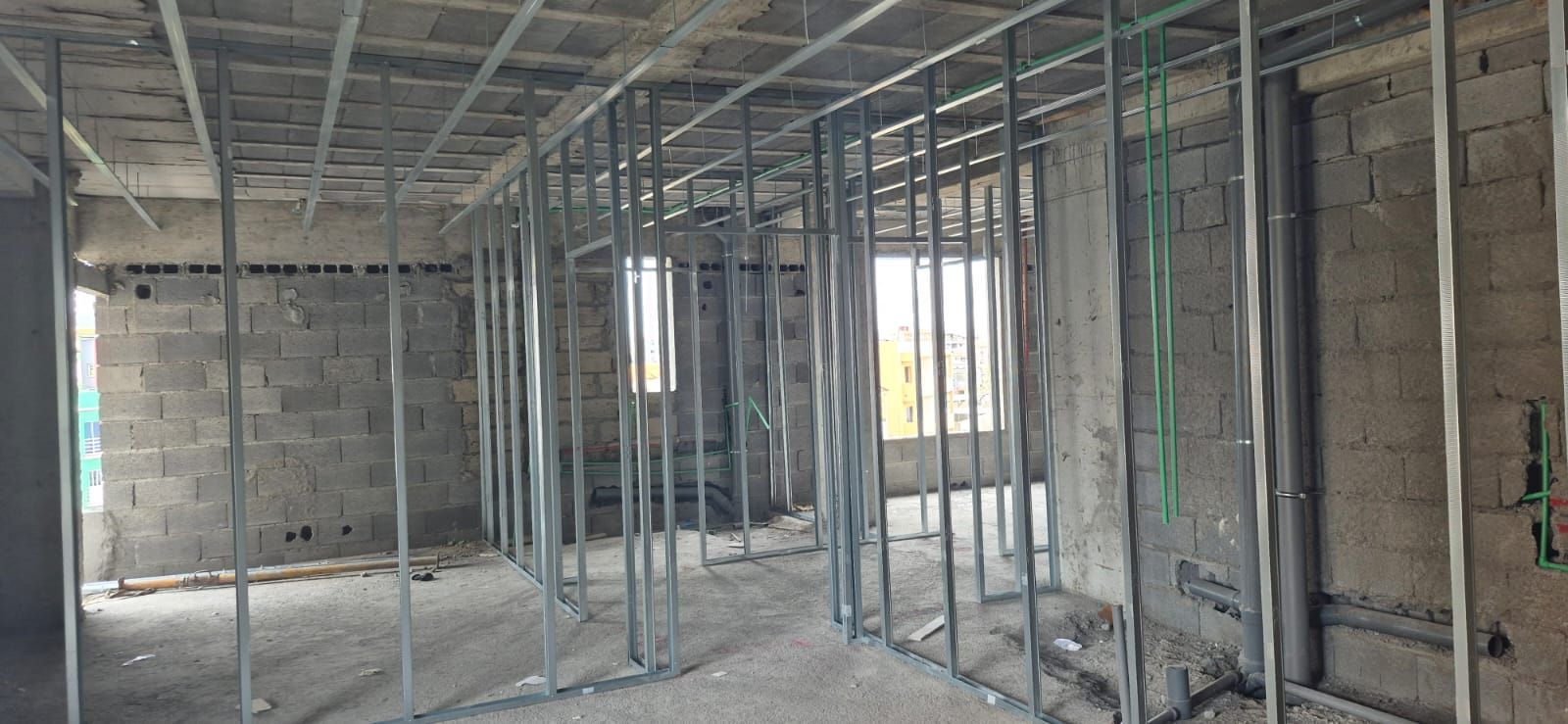 Vista interna de um edifício em construção, com estrutura metálica e paredes de blocos de concreto aparentes.