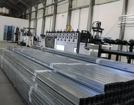 Pilhas de tubos de metal em uma oficina industrial com máquinas ao fundo.